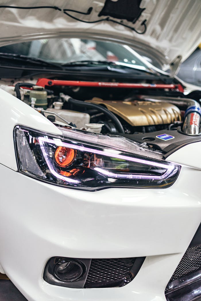 Close-up of a car's engine and headlight under the open hood in a garage.